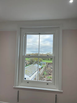 A white-framed window shows an outdoor view of a cloudy sky, green fields, and rooftops