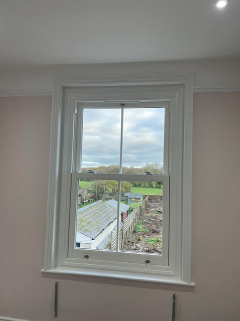 A white-framed window shows an outdoor view of a cloudy sky, green fields, and rooftops