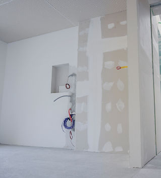 Unfinished interior wall with exposed wires and drywall patches