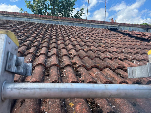 View from a ladder over a dirty, mossy, weathered red pantile roof under a bright blue sky