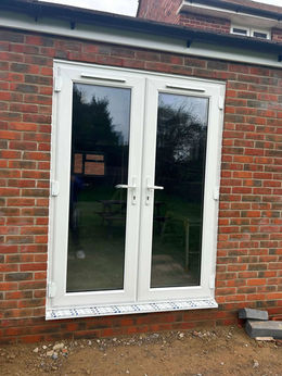 A pair of white French doors set in a red brick wall, showing a garden