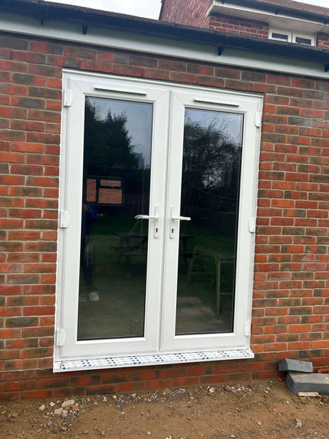 A pair of white French doors set in a red brick wall, showing a garden