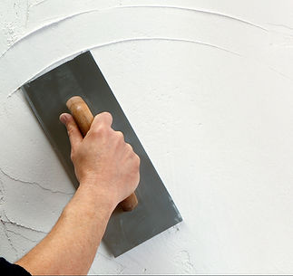 A hand smooths white plaster on a wall using a flat metal trowel