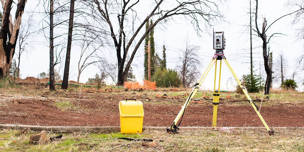 A yellow tripod-mounted surveyor's tool stands on dry grass