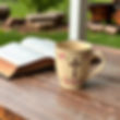 large beige coffee cup with pink floral trim that has a cross on the cup sitting on a rust