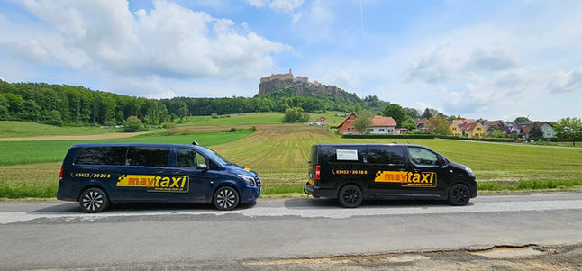 Zwei MayTaxi Leibnitz Minibusse vor Landschaft mit Burg. Start MayTaxi Leibnitz.