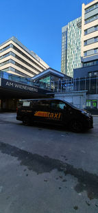 Schwarzes Taxi mit dem Aufdruck MayTaxi Leibnitz vor einem Gebäude