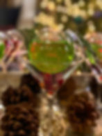 a Christmas ornament filled with a green drink resting on top of cranberries in a martini glass