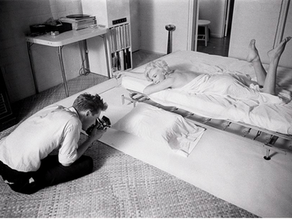 An example of an early boudoir photoshoot. Marilyn Monroe posing in white sheets. Black and white photo showing the photographer Douglas Kirkland working with Monroe. 