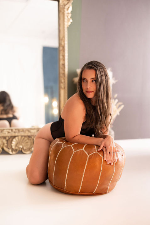 woman glancing aside over a leather pouf, luxury boudoir photo shoot