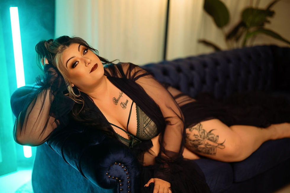 Woman in black robe lounges on a blue couch, hand in hair. Green light glows in the background. Mood is relaxed and confident.