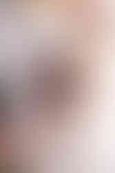 Woman stands next to white wall with flower arch over her in boudoir photography studio. She's wearing dark purple lingerie and her head is raised in confidence.