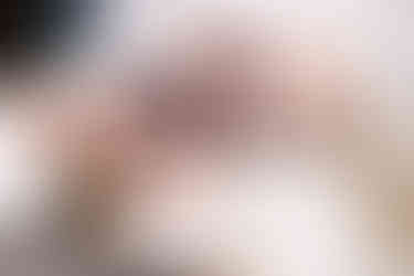 Woman laying on bed and leaning her head off the side. Her arms are up behind her head and she's smiling.