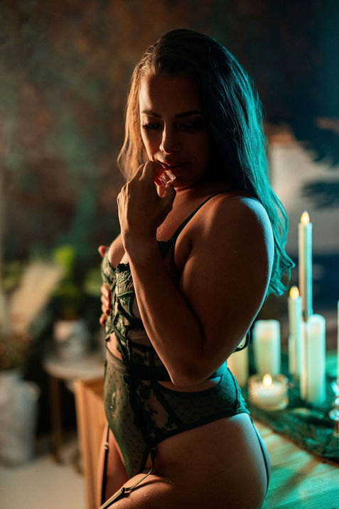 woman in green lace with fingertip at lips in teal candlelight, boudoir photo