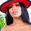 Thumbnail: Woman wearing a black hat with red brim posing for a photo. Madame Curves