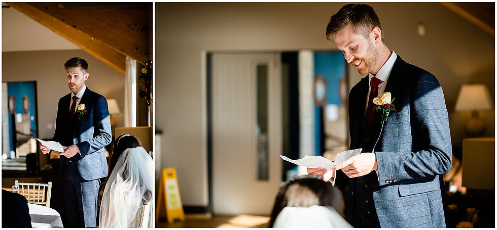Groom in navy suit reads vows from paper at an indoor wedding, smiling as the veiled bride sits nearby in warm light