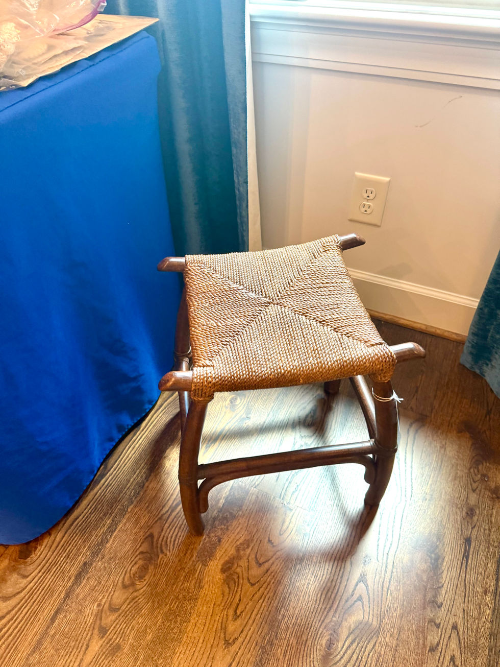 Woven stool on wooden floor near blue curtain.