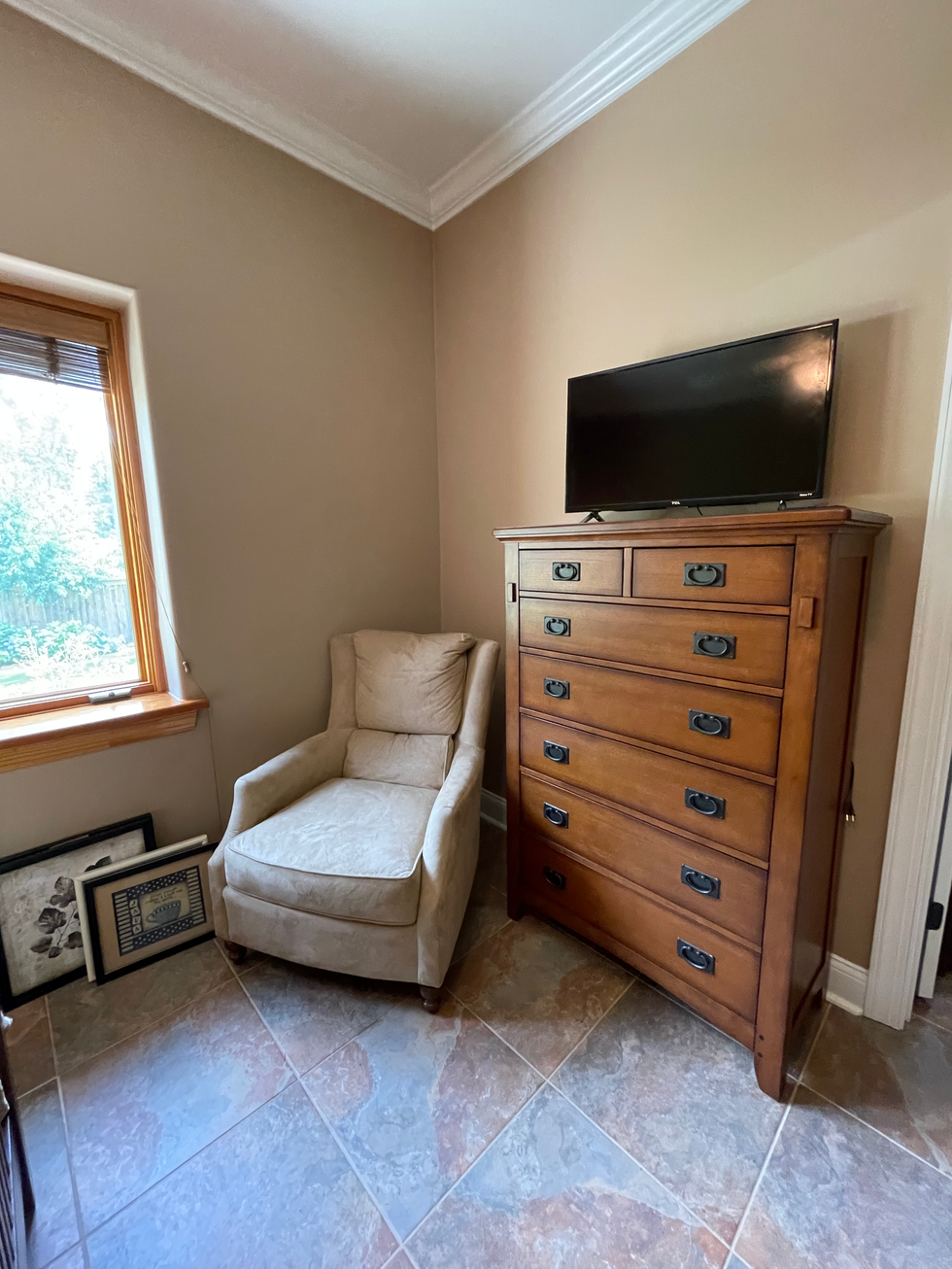 a chair sits next to a dresser with a flat screen tv on top of it