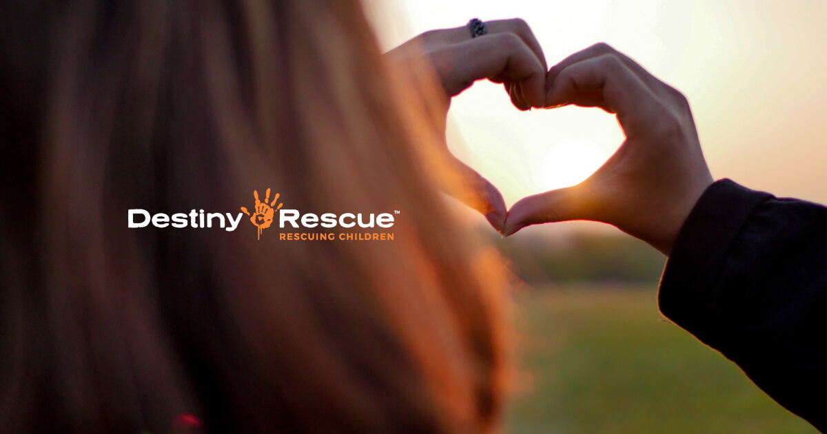 Destiny Rescue logo over hands forming a heart at sunset