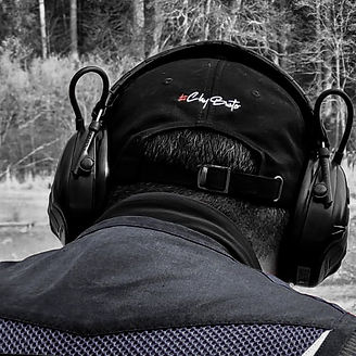 Clay Buster cap worn at shooting range with ear protection, highlighting refined branding and shooting lifestyle