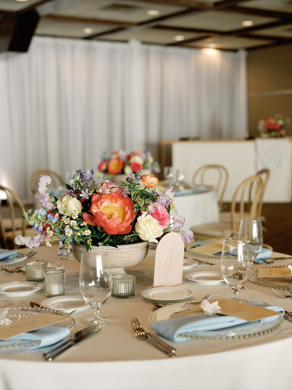 Elegant banquet table with pastel napkins, glassware, and a colorful floral centerpiece design by sarasota floral designer tailored twig; table number 4 in a soft-lit event hall. Best Sarasota wedding planner jennifer matteo