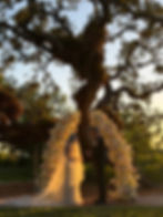 Bride and groom standing under full arch of white flowers in the sunset for wedding at marie selby botanical gardens