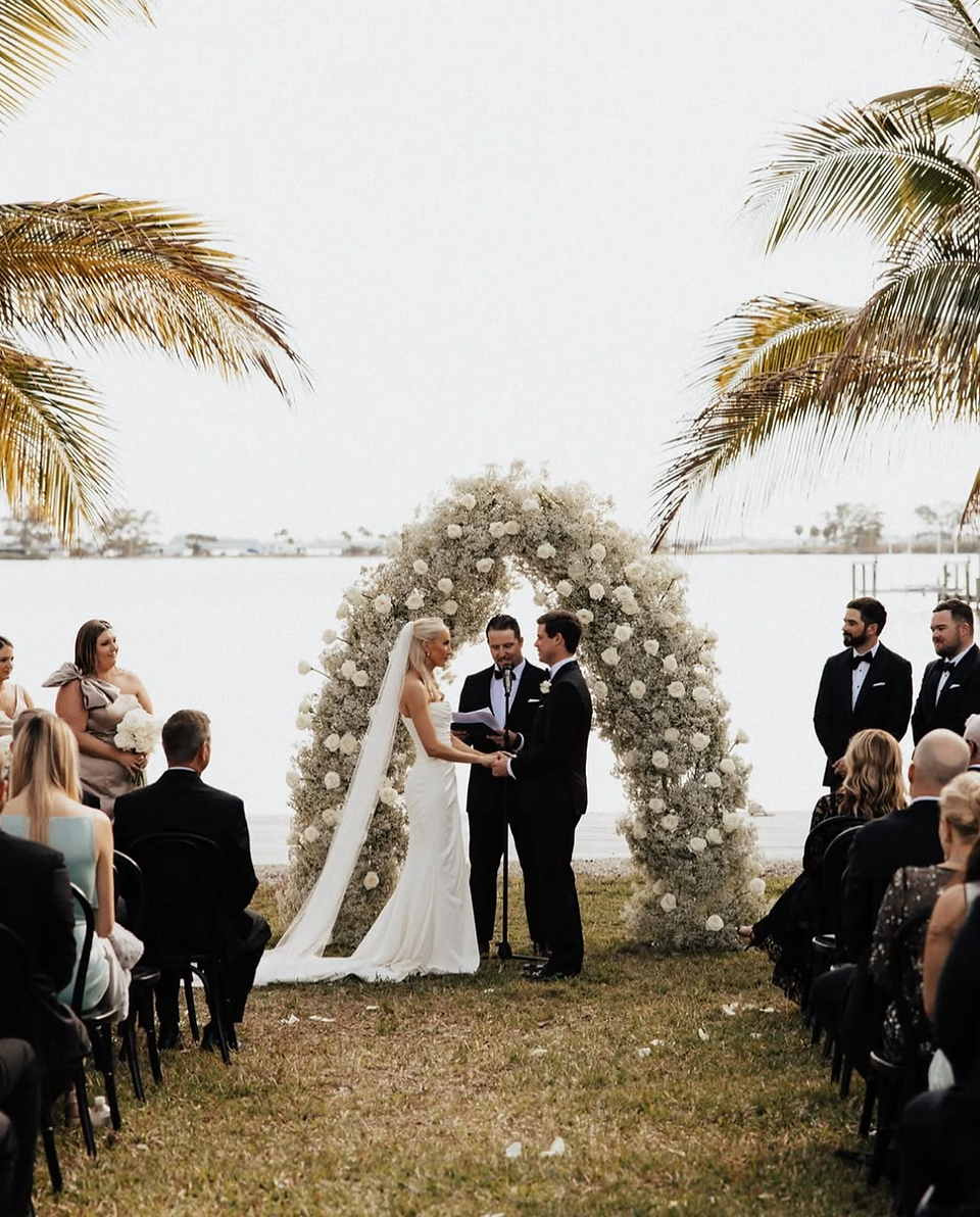 bride and groom underneath a white rose arch saying i do while overlooking sarasota bay