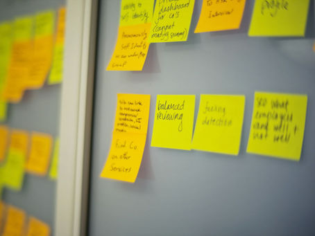 Yellow and orange sticky notes with handwritten notes stuck to a gray wall