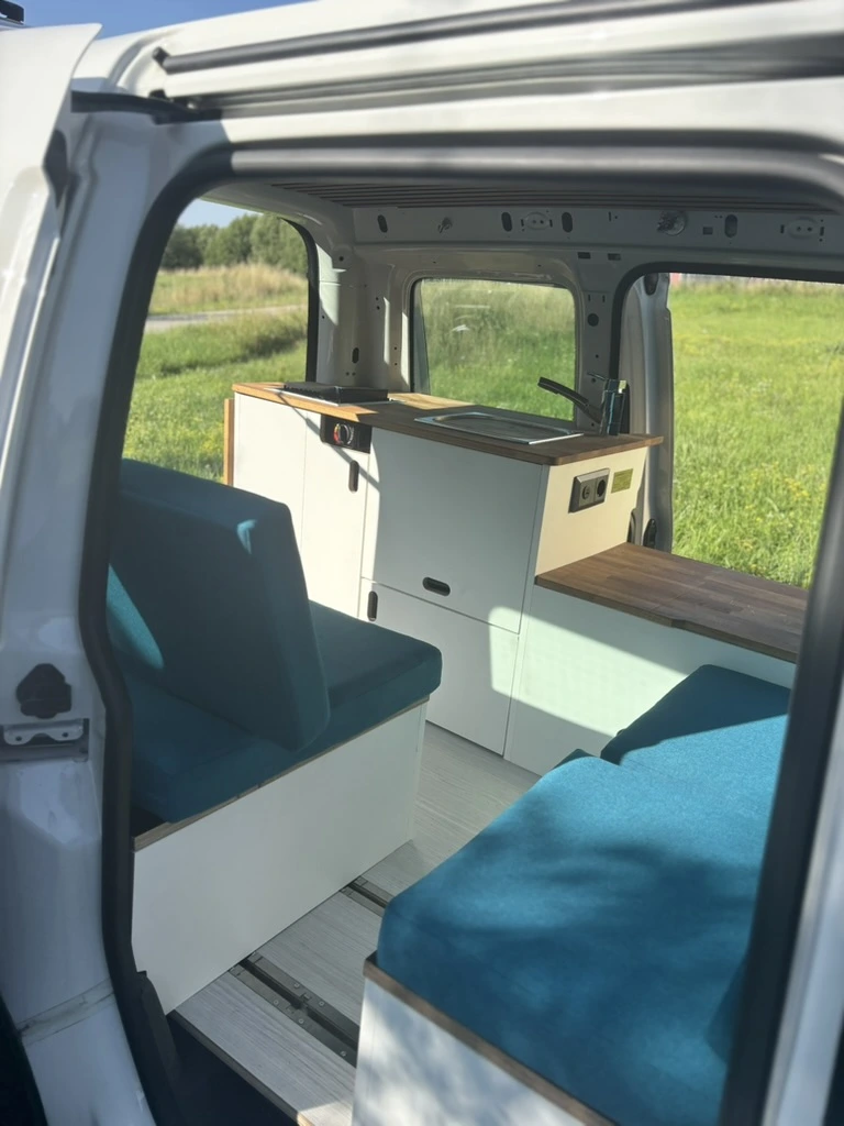 Caddy Camper mit aufgebautem Bett und geöffneter Seitentür auf einer Wiese