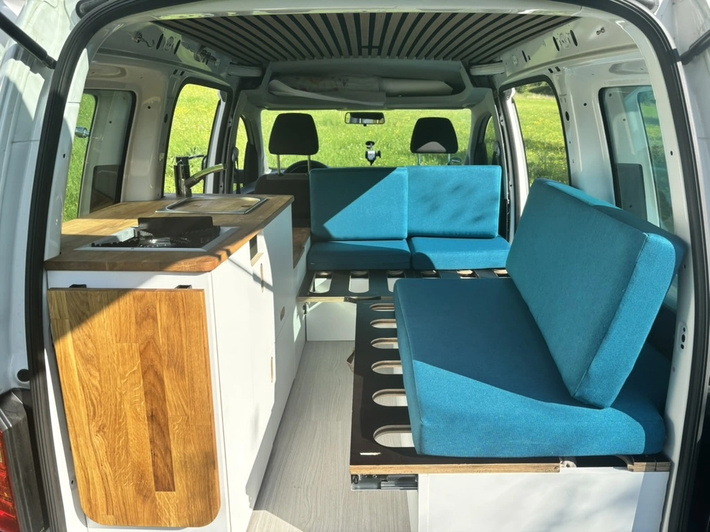 Fertiger VW Caddy Camper mit geöffneter Heckklappe und Blick auf das Bett
