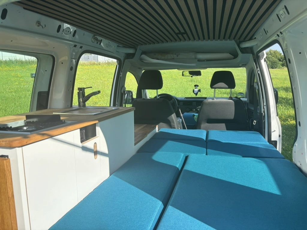 Fertiger VW Caddy Camper mit geöffneter Heckklappe und Blick auf das Bett