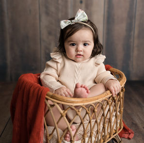 Baby girl sitting in a cradle during a six month milestone photo session in a Corpus Christi photography studio