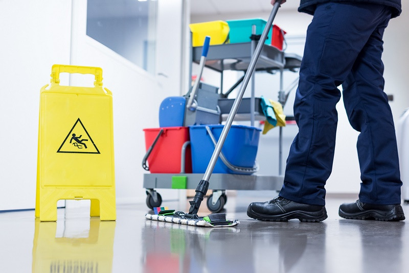 Janitor with Mop and Bucket Standing Next to Slip Caution Sign