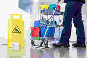 Janitor with Mop and Bucket Standing Next to Slip Caution Sign