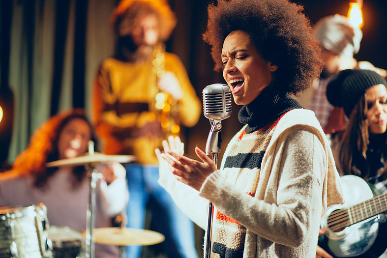 Close up of mixed race woman singing. In background band playing instruments. Home studio