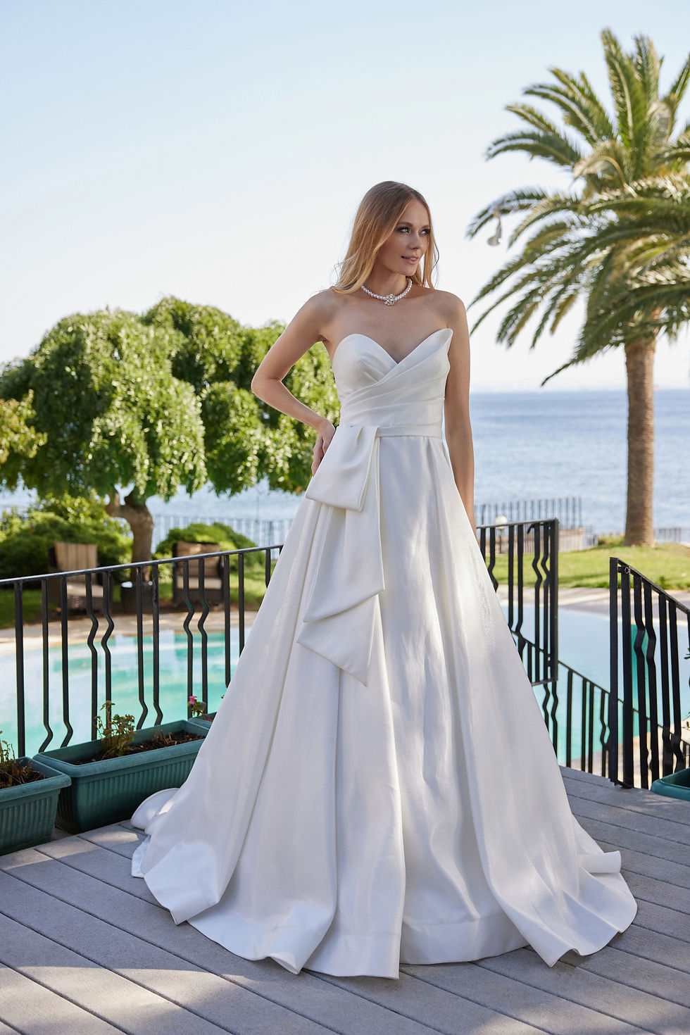 Gövdesi drapeli, straplez yaka ve mimari fiyonk kemer detaylı modern saten gelinlik modeli.