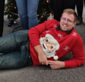 Man lying on the floor wearing a red Christmas jumper with a picture of Santa