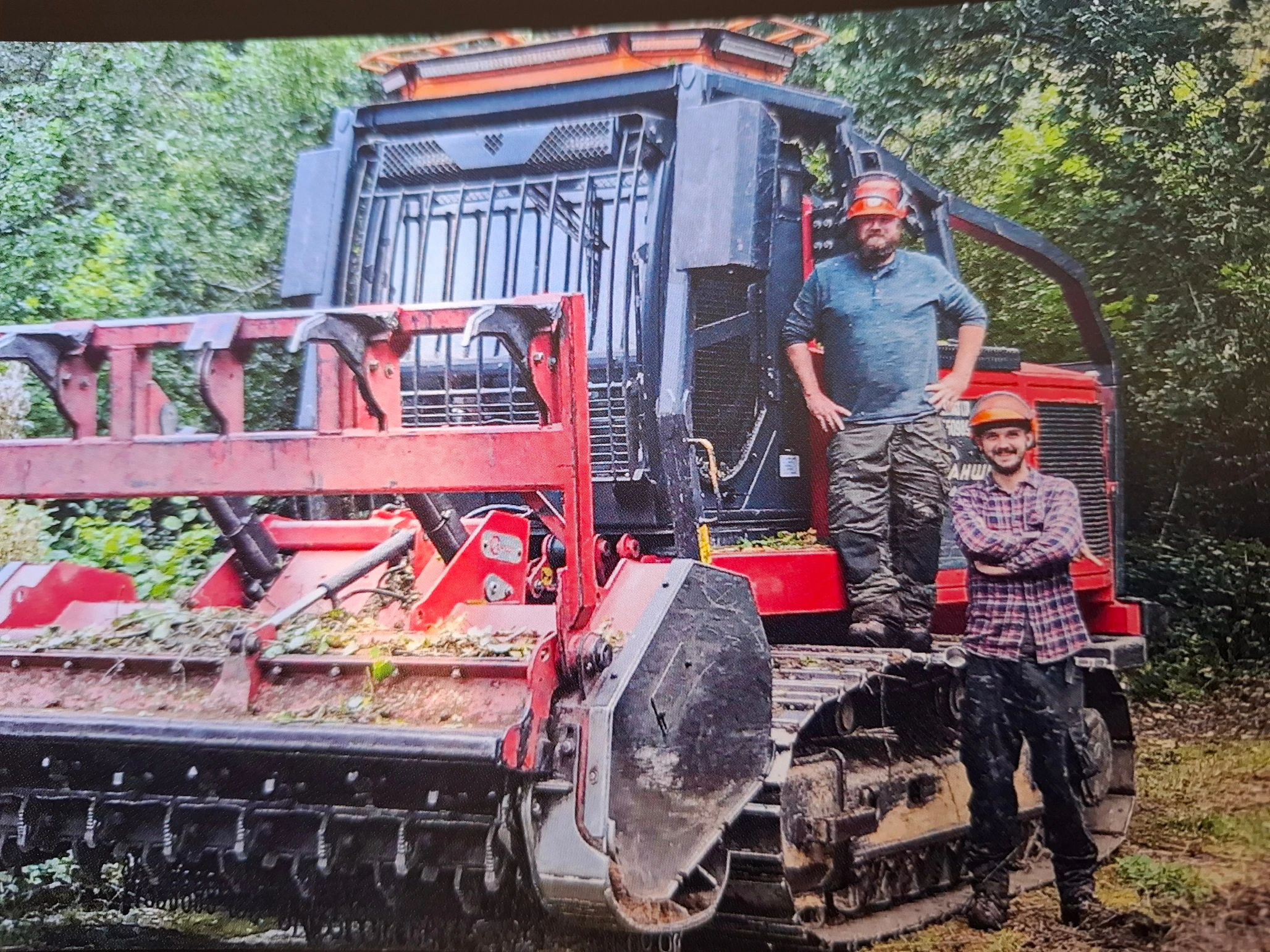 Two men and a red stump grinding machine.