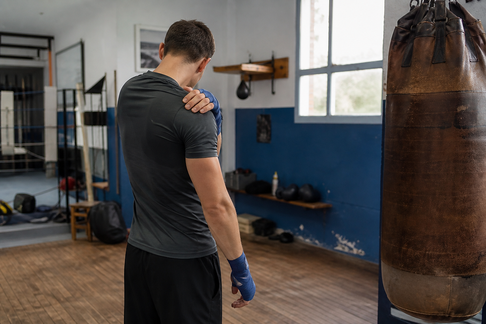 Boxeur amateur touchant son épaule douloureuse après un entraînement au sac de frappe