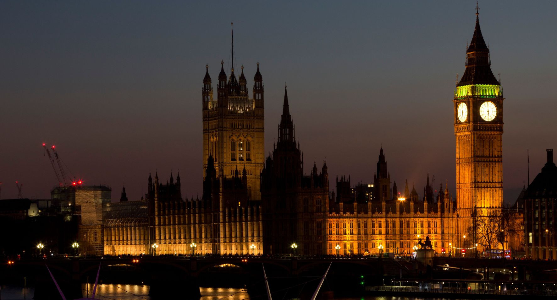 Verlicht Westminster en Big Ben bij nacht, met de Theems en brugreflecties onder een donkere hemel.