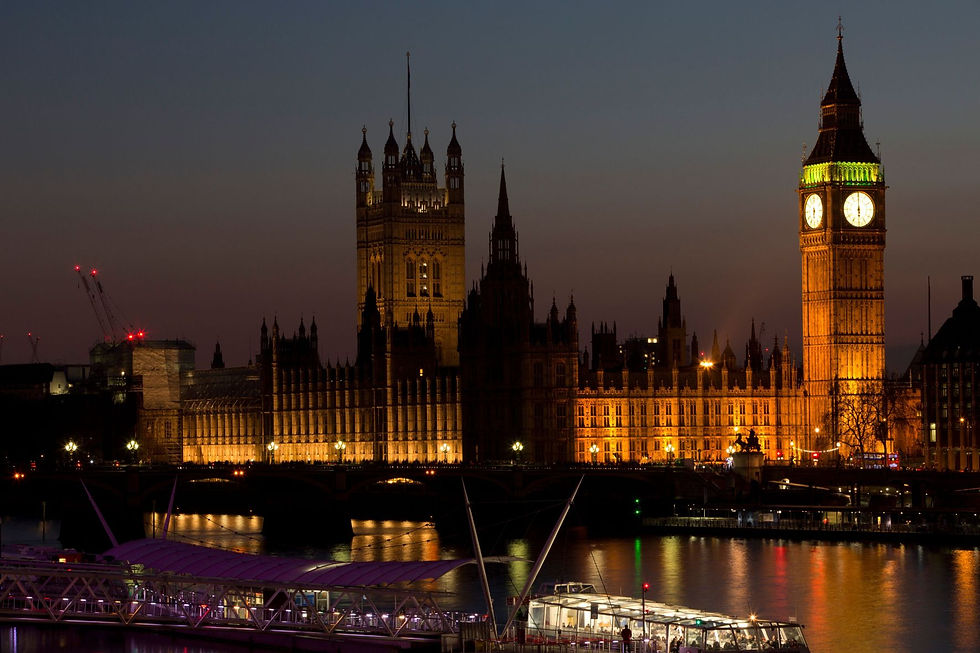 Verlicht Westminster en Big Ben bij nacht, met de Theems en brugreflecties onder een donkere hemel.