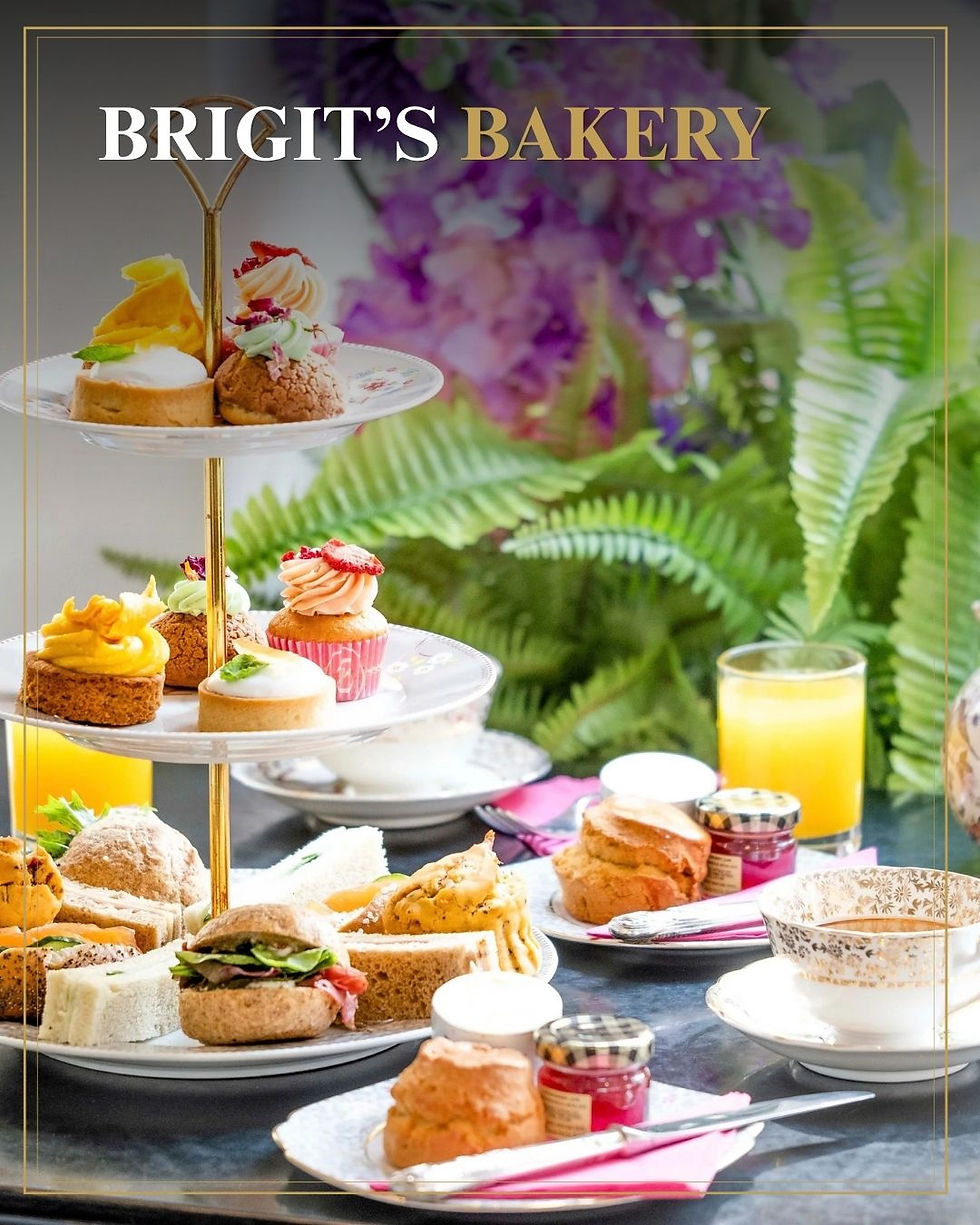 Luxe etagère met taartjes, sandwiches, scones en jus bij BRIGIT’S BAKERY, met bloemen en varens op de achtergrond.