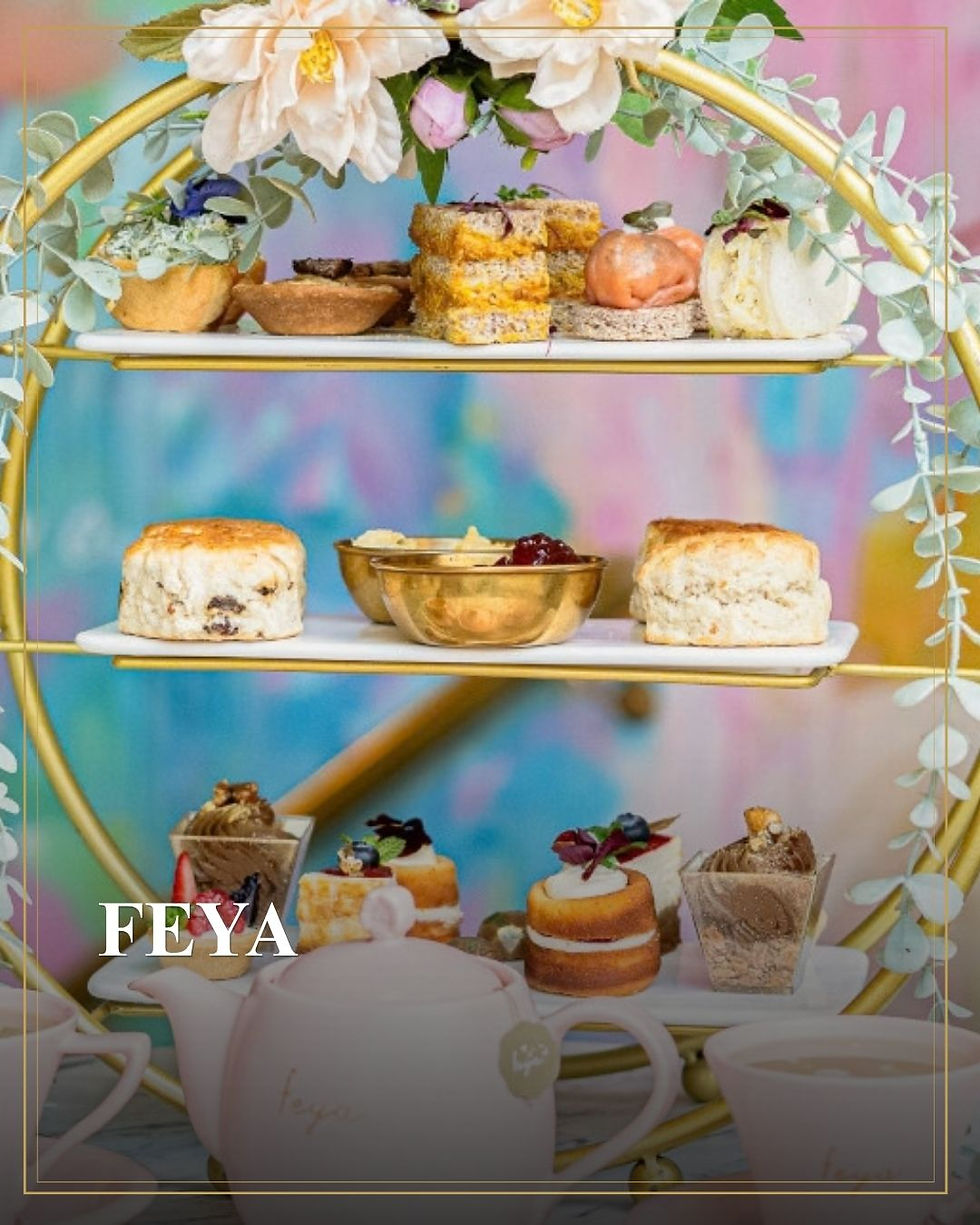 Pastelkleurige etagère met taartjes en theepot; bloemendecoratie en FEYA op de voorgrond.