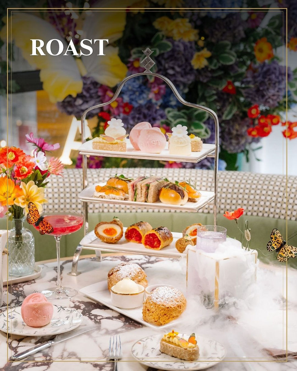 Luxe high tea met zoete hapjes op etagère, bloemenwand en rook op marmeren tafel; tekst ROAST.