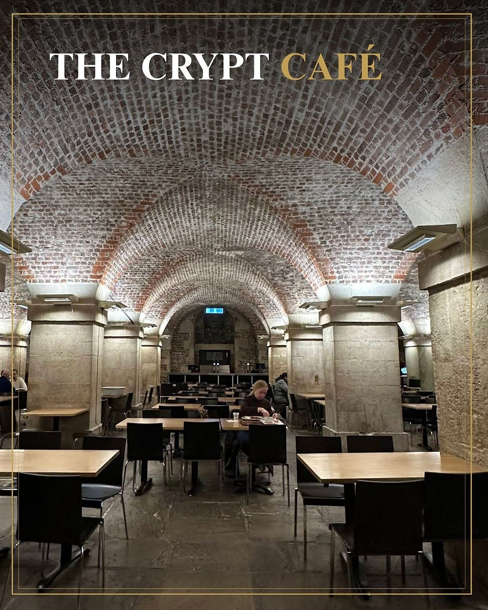 Ondergrondse cryptcafé met bakstenen gewelven, lege tafels en enkele gasten; tekst: THE CRYPT CAFÉ.