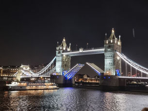 Tower Bridge in Londen bij nacht met openstaande brugdekken, verlicht in blauw en wit. Een boot vaart voorbij op de rivier.