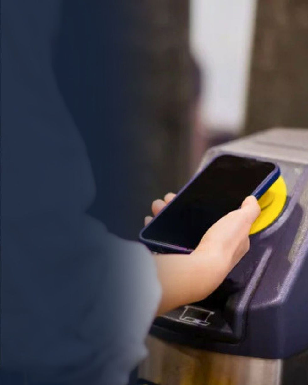 Persoon houdt smartphone tegen gele contactloze lezer op een poortje, klaar om in te checken.