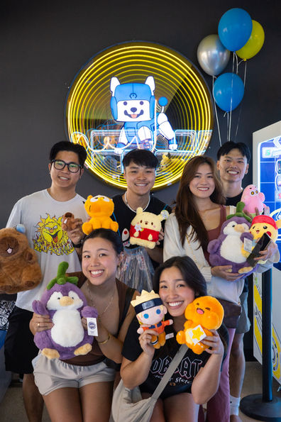 Six people smiling and holding up prizes in front of a mirror with a blue mechanical dog
