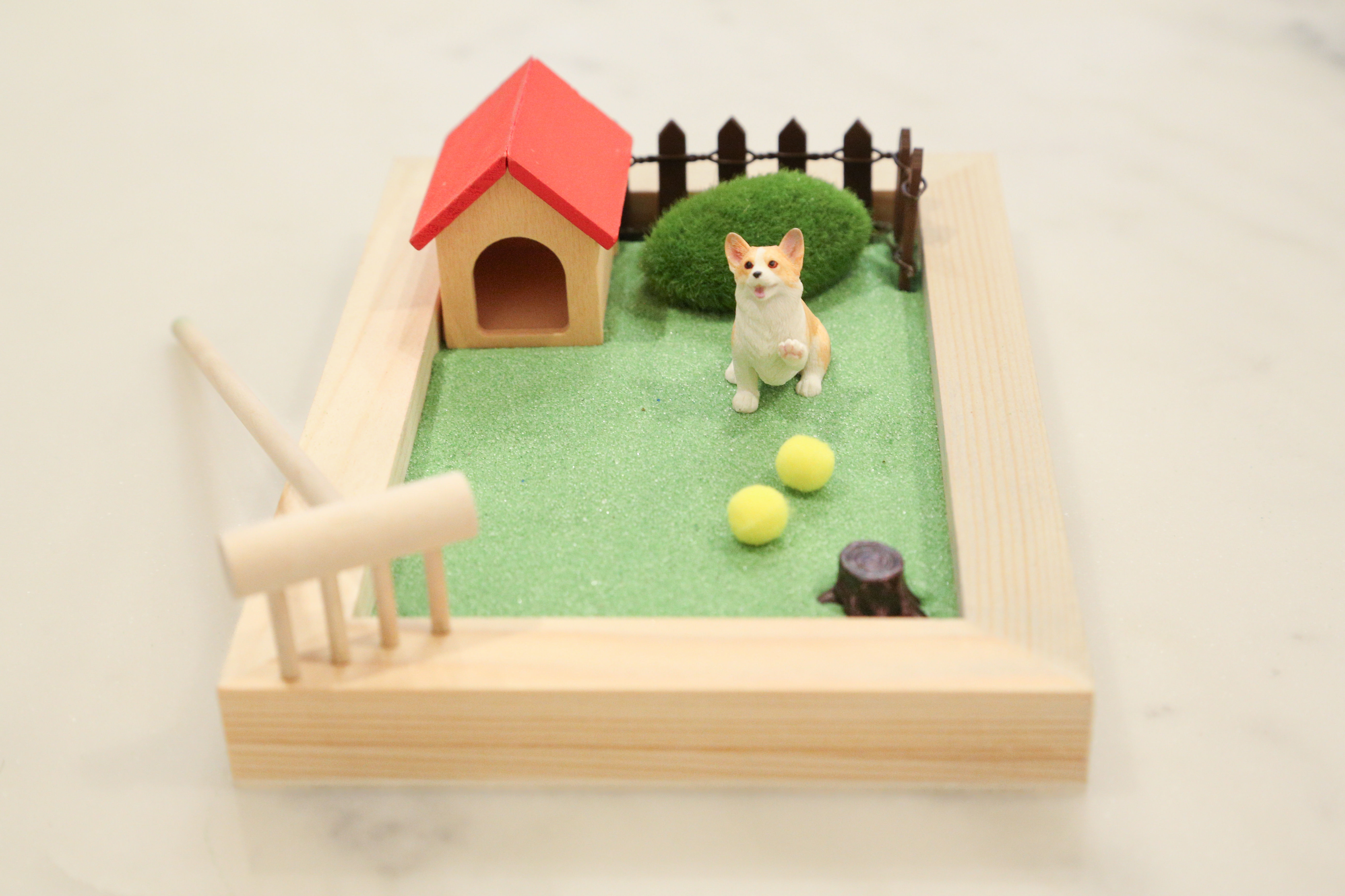 Miniature dog figurine in a wooden frame with a small house and balls.