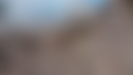 An aerial view of stone built fortifications perched on a rocky, barren cliff above a frothy sea.